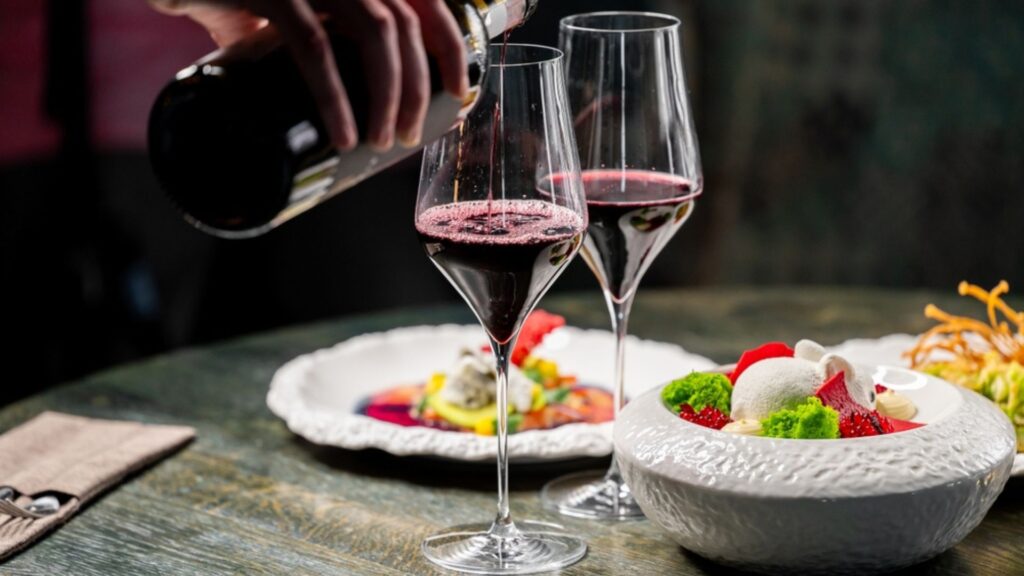 Two glasses of Italian red wine and a bottle pouring, pairing with a tomato and mozzarella caprese salad