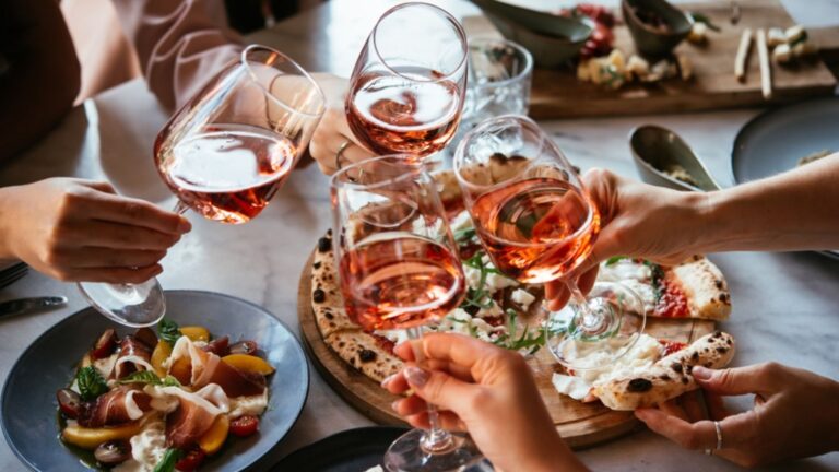 A toast with four glasses of Italian rosé wine pairing with pizza over a table